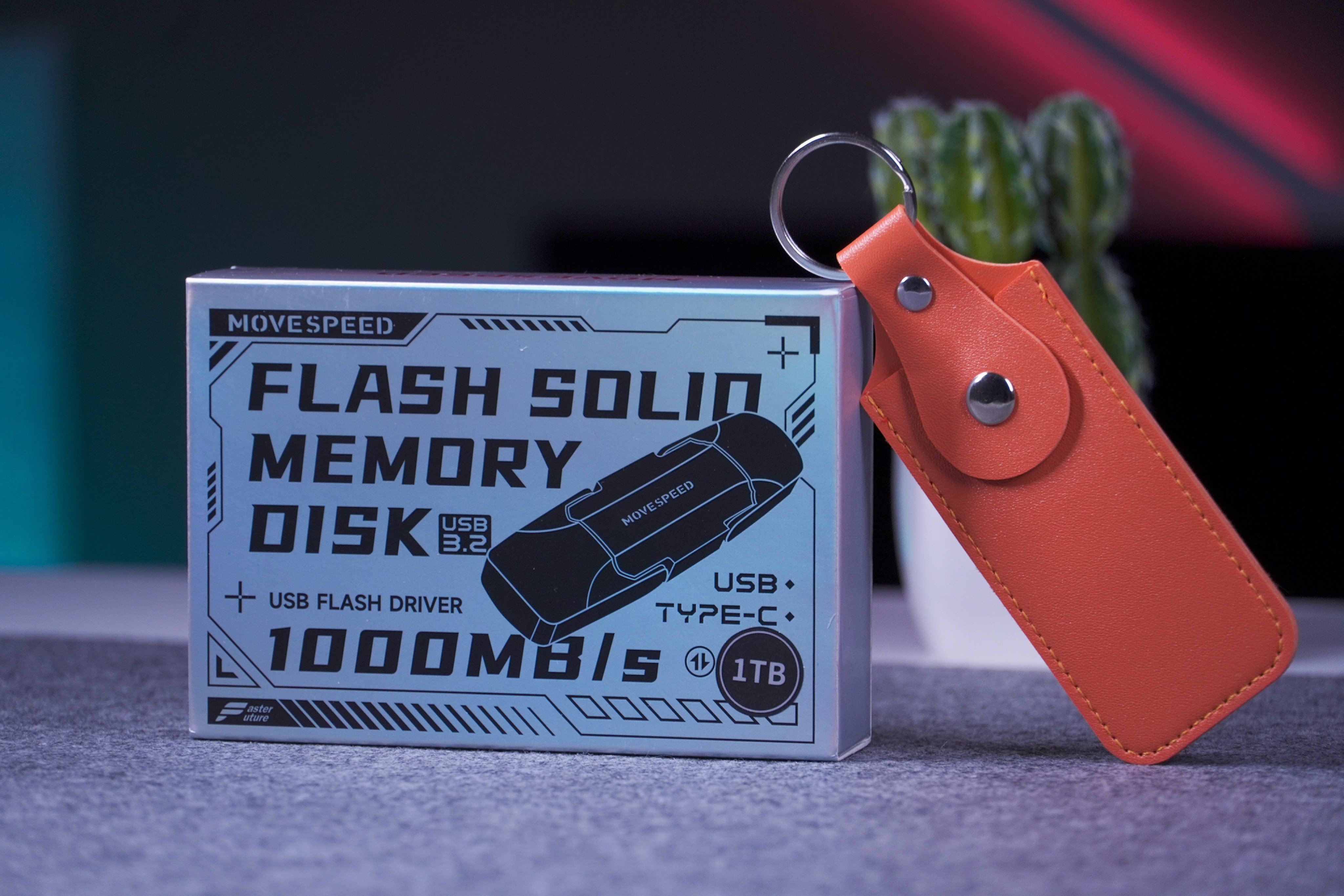 علبة ذاكرة MoveSpeed بسعة 1TB بجانب حافظة برتقالية وحلقة مفاتيح.